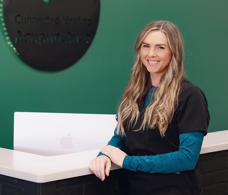 Smiling woman at acupuncture reception desk.